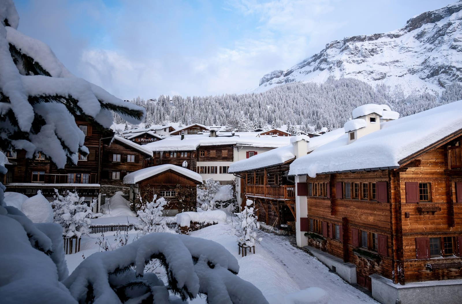 Tief verschneite Holzchalets in einem Bergdorf unter felsigem Gipfel