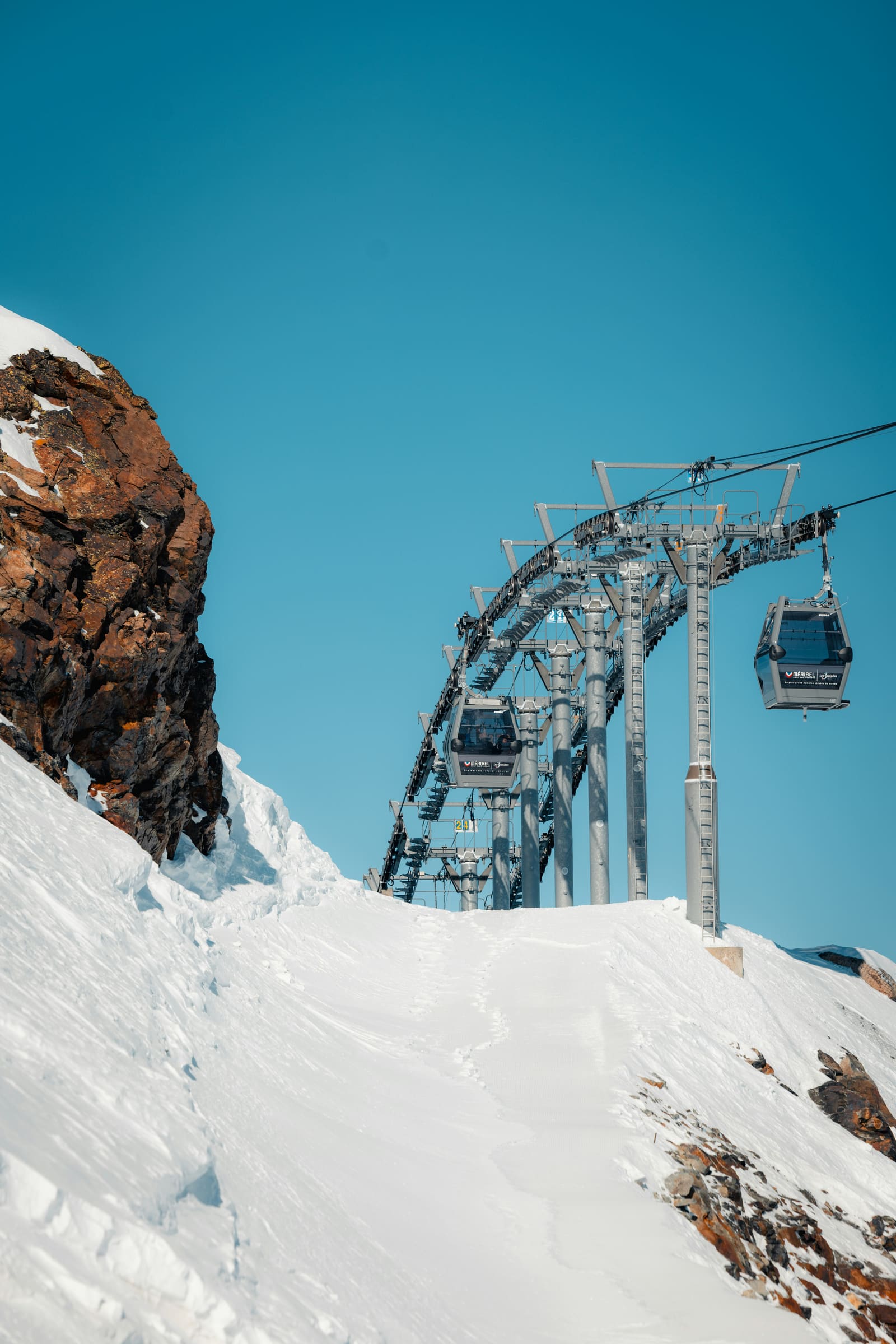 Moderne Gondelbahn mit Kabinen über einem verschneiten Grat vor tiefblauem Himmel