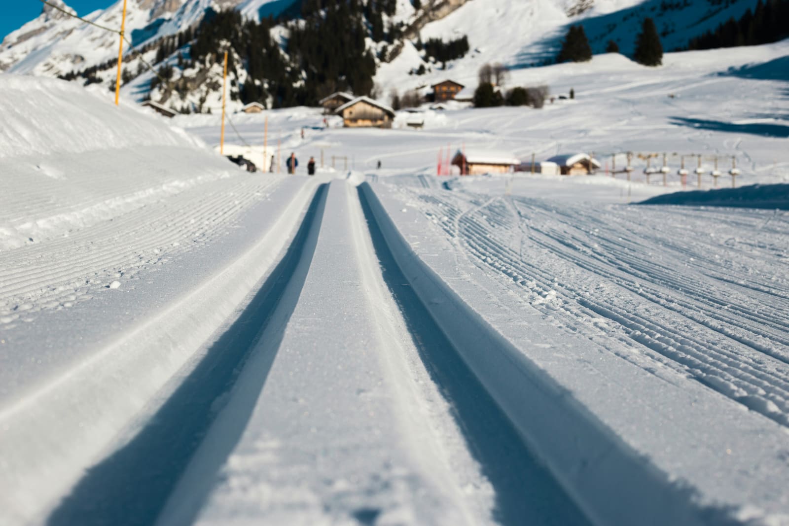 Frisch gespurte Langlaufloipe führt durch ein sonniges Tal zu Holzchalets